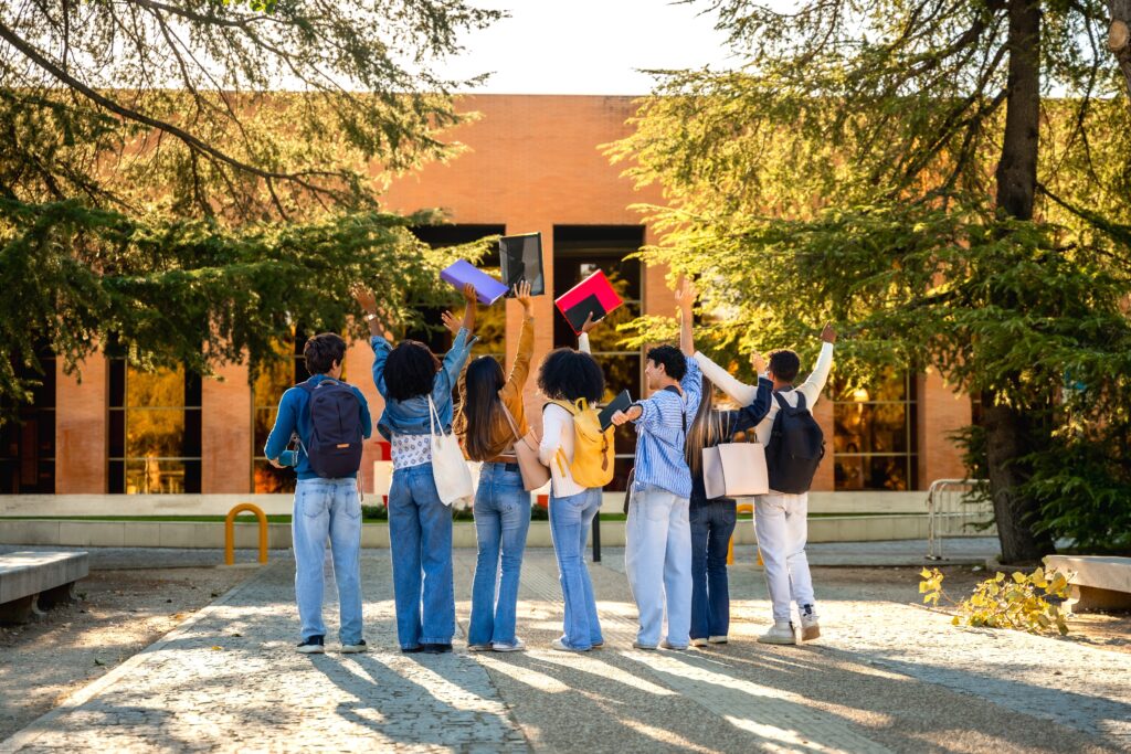diverse students celebrating success throwing notebooks on campus
